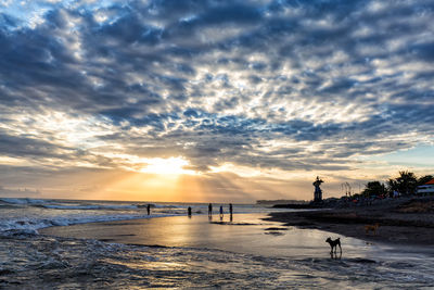 Silhouette people on shore at beach against sky during sunset