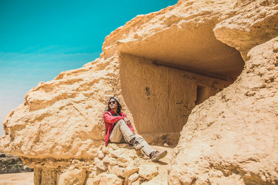 Woman sitting on rock against sky