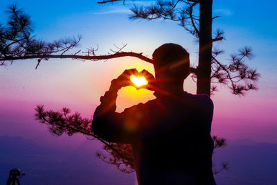 Silhouette woman photographing against sky during sunset