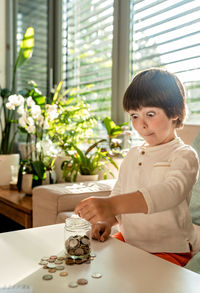 Little toddler boy with surprised face counting money putting coins into glass jar. kid saving 