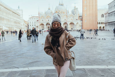 Portrait of woman walking at town square against historic buildings