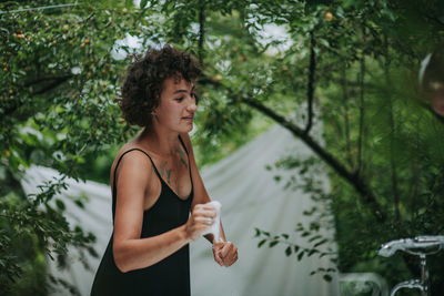 Young woman looking away while standing against plants