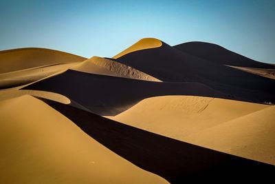 Low angle view of sand dunes against clear sky