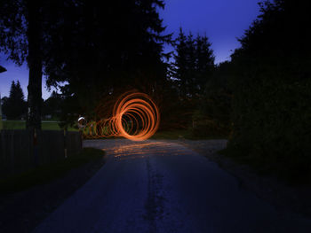 Light trails on road amidst trees against sky at night