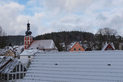 Snow covered houses by building against sky