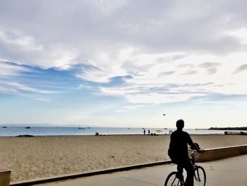 Man riding bicycle on footpath against beach