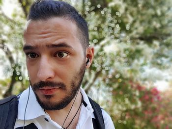 Portrait of young man listening music against tree