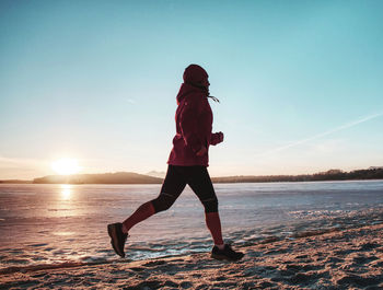 Running sport woman. female runner jogging at cold winter bay wearing warm sporty running clothing