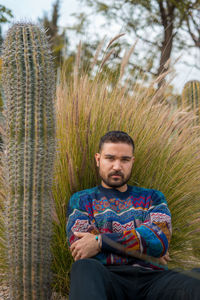 Young moroccan model sitting on the ground in a public park next to a big cactus