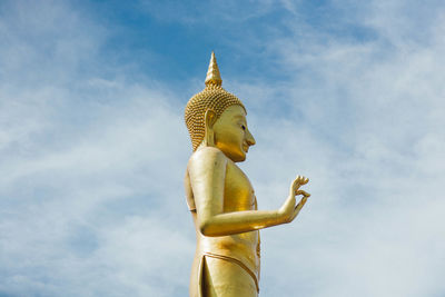 Low angle view of golden buddha statue against sky