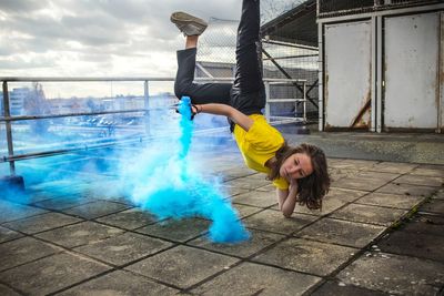 Young woman with smoke bomb doing breakdancing on roof