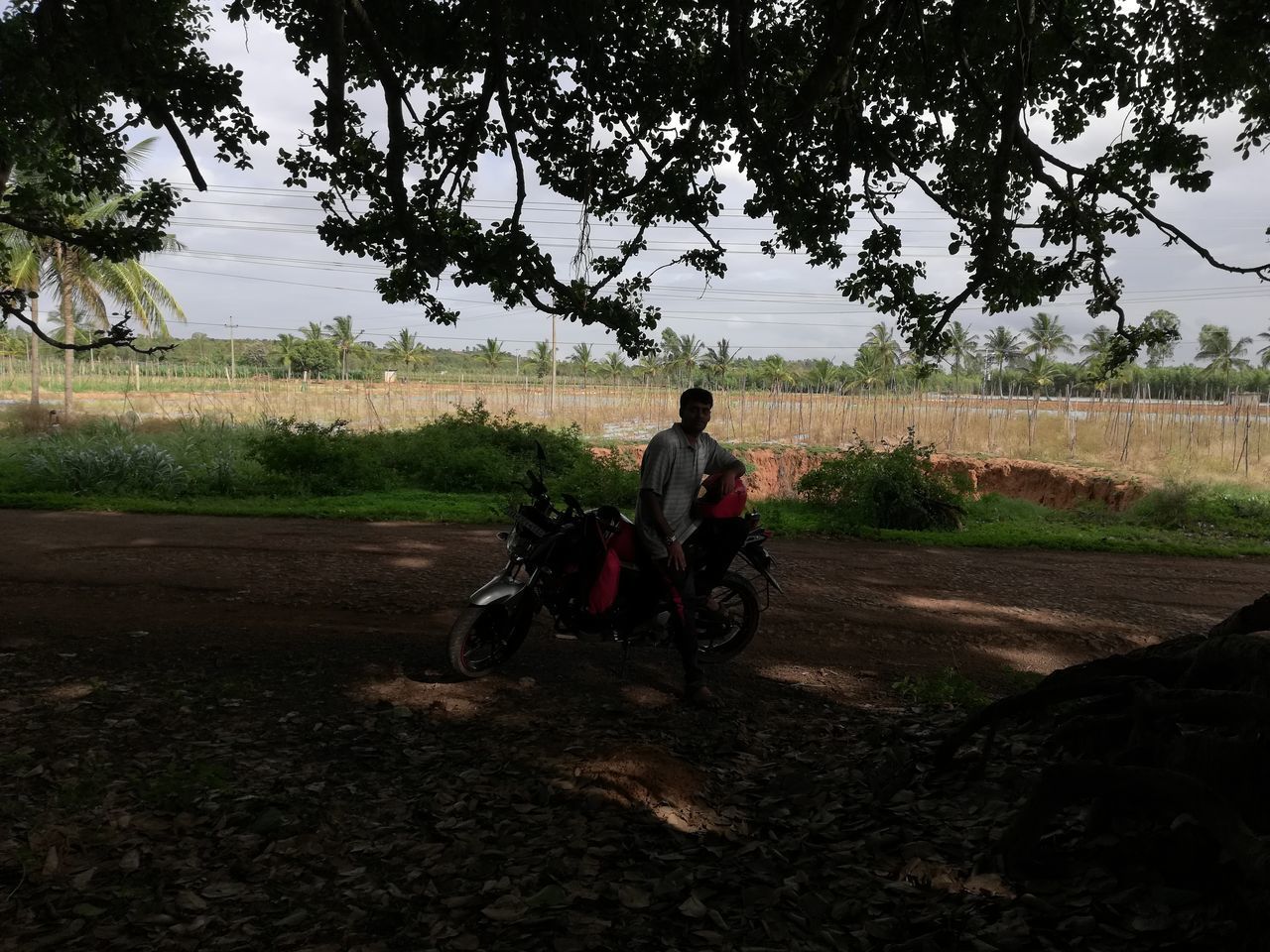 MAN RIDING MOTORCYCLE ON ROAD BY FIELD