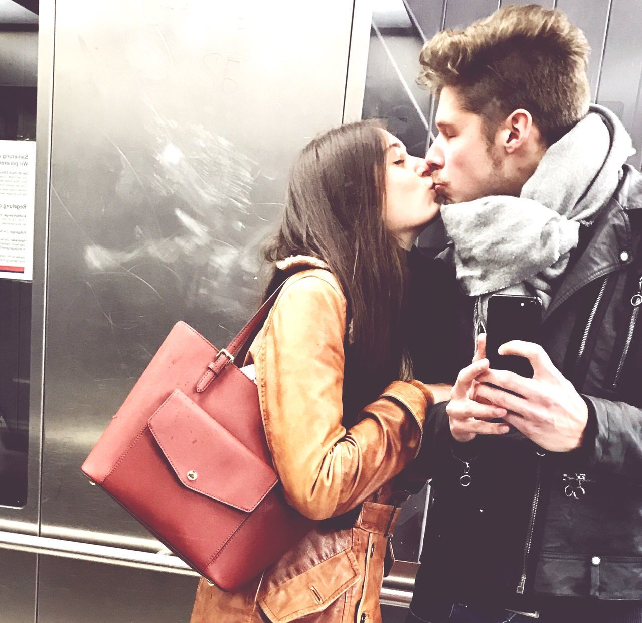 two people, young adult, young men, togetherness, real people, young women, love, transportation, lifestyles, young couple, public transportation, portable information device, holding, side view, technology, wireless technology, couple - relationship, men, day, bonding, warm clothing, outdoors, close-up, people