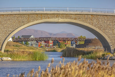 Arch bridge over river by buildings against sky