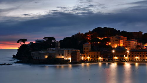 Illuminated buildings by lake against sky at dusk