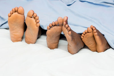 This family lying in bed show their bare feet and half covered