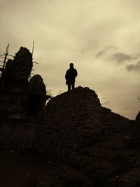 Low angle view of man standing on rock against sky