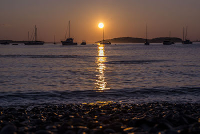 Sailboats in sea at sunset