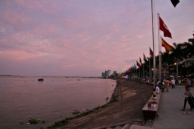 People on street by sea against sky during sunset