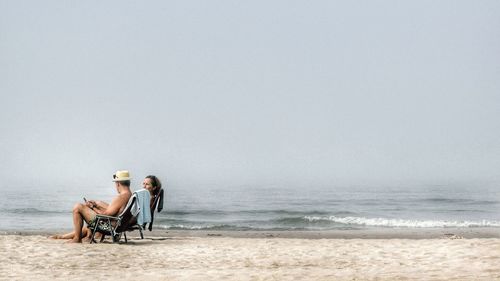 Men sitting on shore at beach against sky