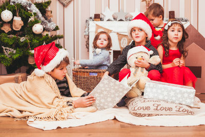 Brothers and sisters sitting by christmas tree