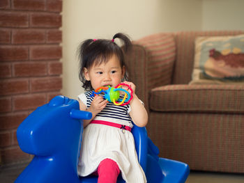 Girl holding toy while playing on rocking horse at home