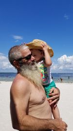 Midsection of shirtless man standing by sea against sky