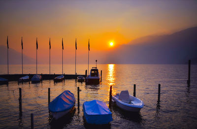 Sailboats moored in sea against sky during sunset