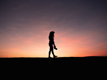 Silhouette woman walking on land against sky during sunset