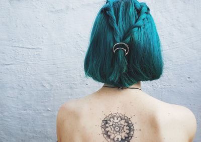 Rear view of shirtless woman with dyed hair against wall