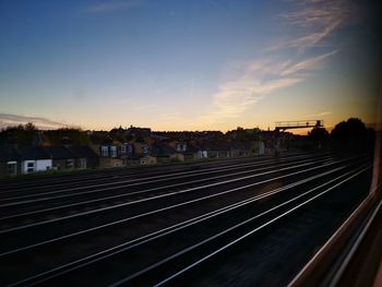 Railroad tracks by buildings against sky during sunset