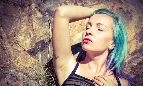 High angle view of young woman with dyed hair resting on rocks during sunny day