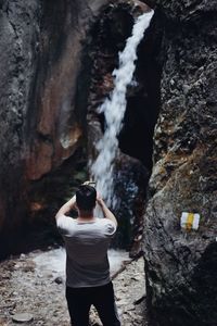 Rear view of man photographing waterfall through smart phone