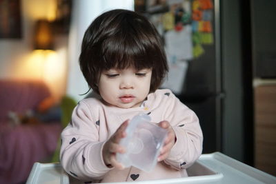 Close-up of cute baby girl holding container sitting at home