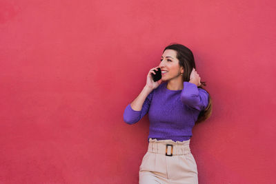 Full length of a smiling young woman standing on pink wall