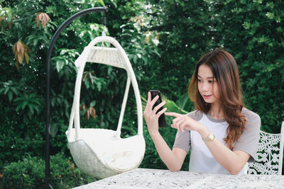 Young woman using smart phone sitting by plants outdoors