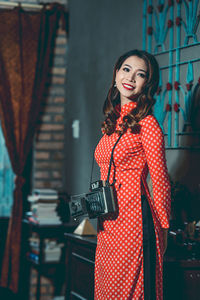Smiling young woman with vintage camera standing at home