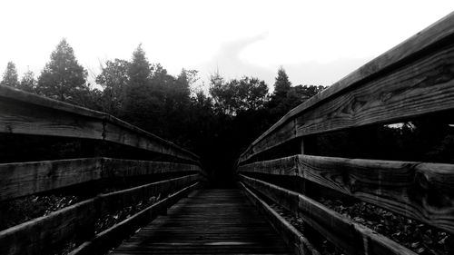 Footbridge amidst trees against sky