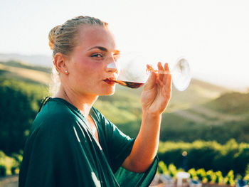 Portrait of woman drinking wine against landscape