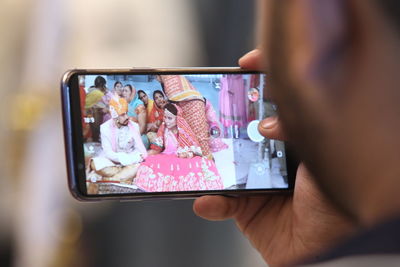 Cropped hand of young man photographing wedding with mobile phone