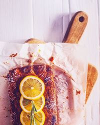 High angle view of cake served with lemon over paper on cutting board