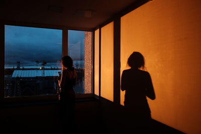 Rear view of silhouette woman looking through window