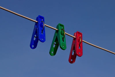 Low angle view of clothespins hanging on rope against blue sky