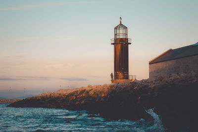Lighthouse by sea and buildings against sky