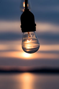 Close-up of light bulb against sea during sunset