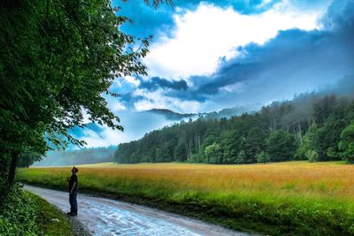 Man walking on field against cloudy sky