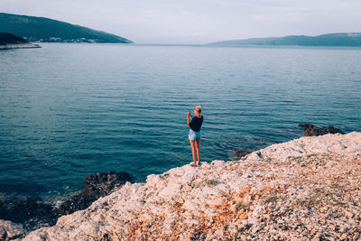 Full length of woman standing on rock by sea against sky