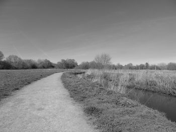 Empty road amidst field against sky