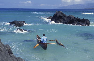 Man rowing outrigger on sea against rock formation