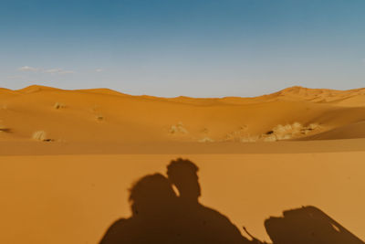 People on sand dune in desert against sky